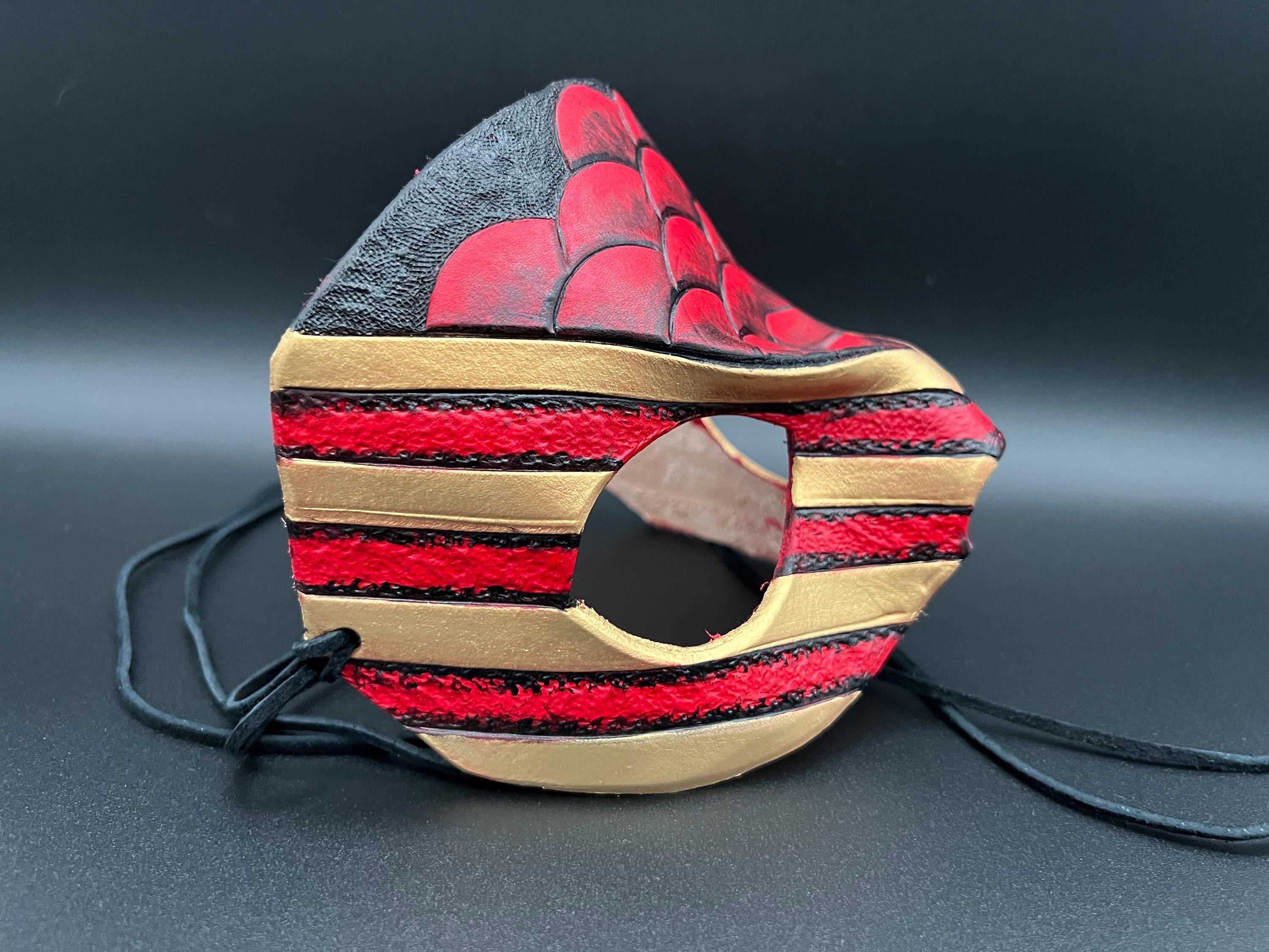 A leather mask featuring a red and black scales design with gold trim dragon motif shown on a dark gray background with black ties