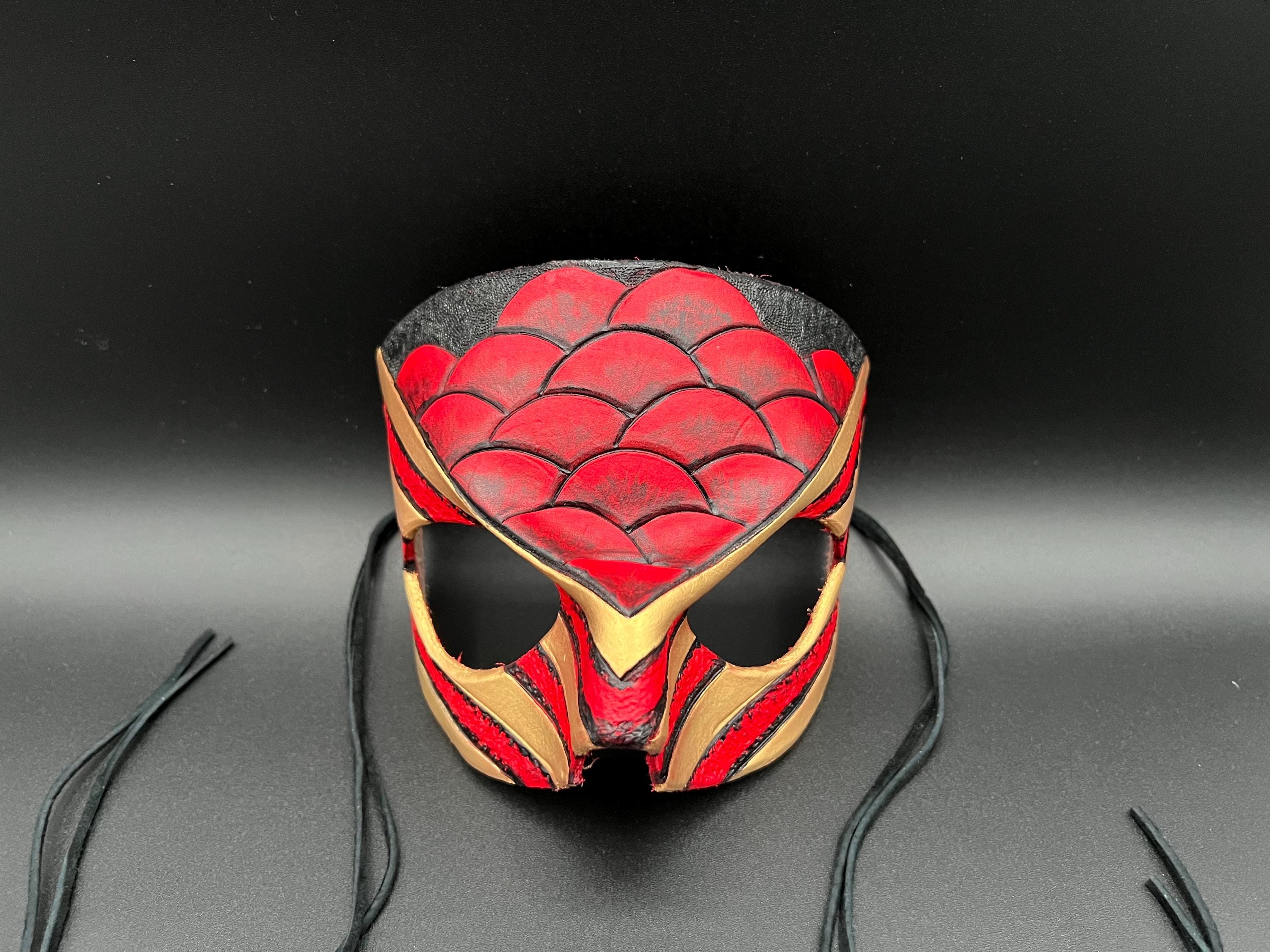 A leather mask featuring a red and black scales design with gold trim dragon motif shown on a dark gray background with black ties