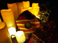 A decorative woven basket or lantern with red, gold, and black stripes sits among glowing candle-like lights in a dark setting.