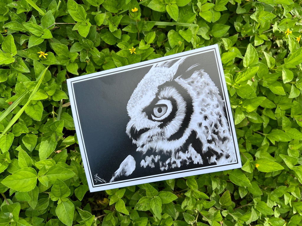 A rectangular art print featuring a black and white detailed illustration of an owl, placed on a bed of green grass.