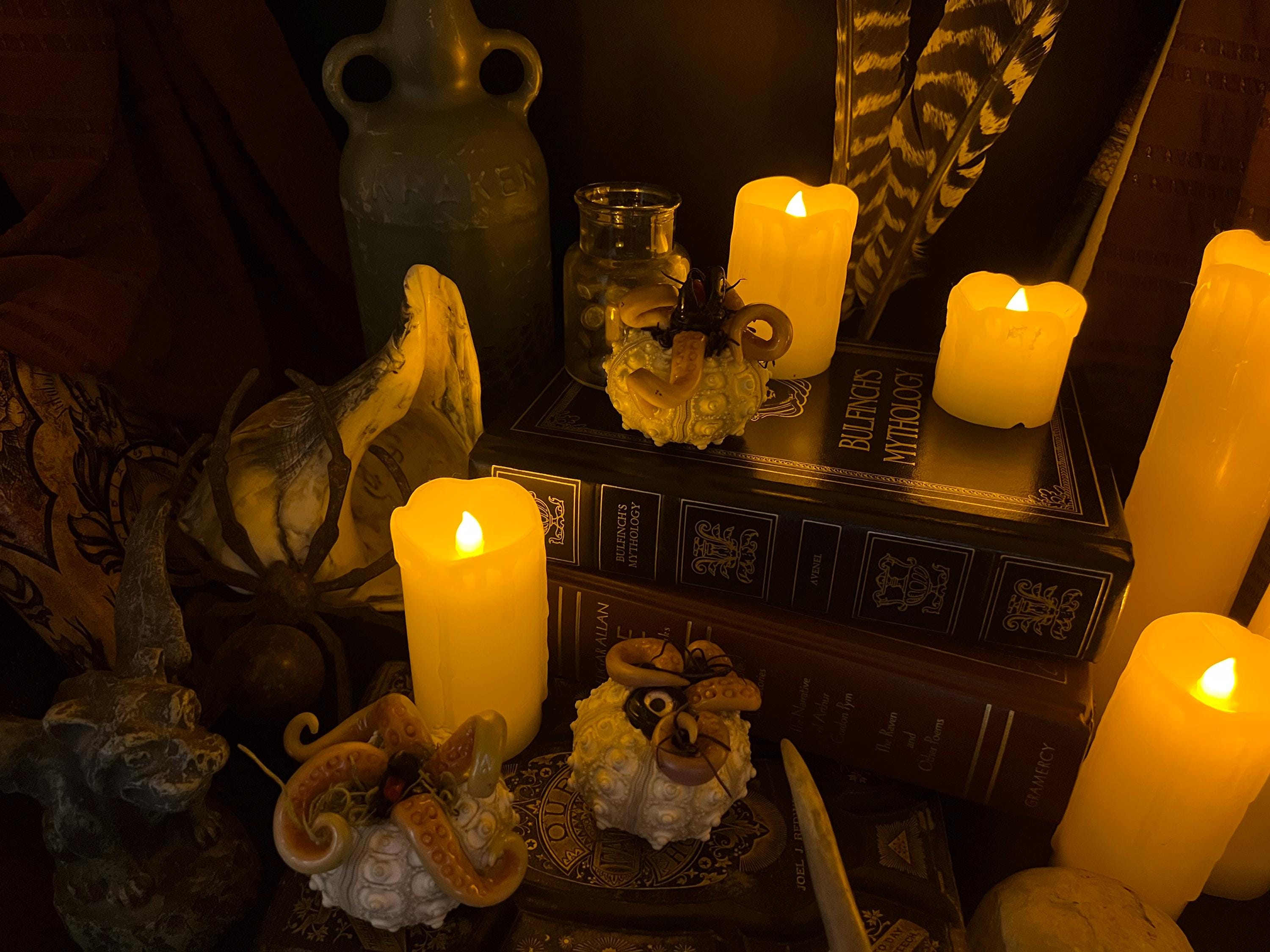 A moody, dark-themed arrangement featuring multiple glowing yellow pillar candles, seashell decorations, a small glass jar, and stacked antique-style books.