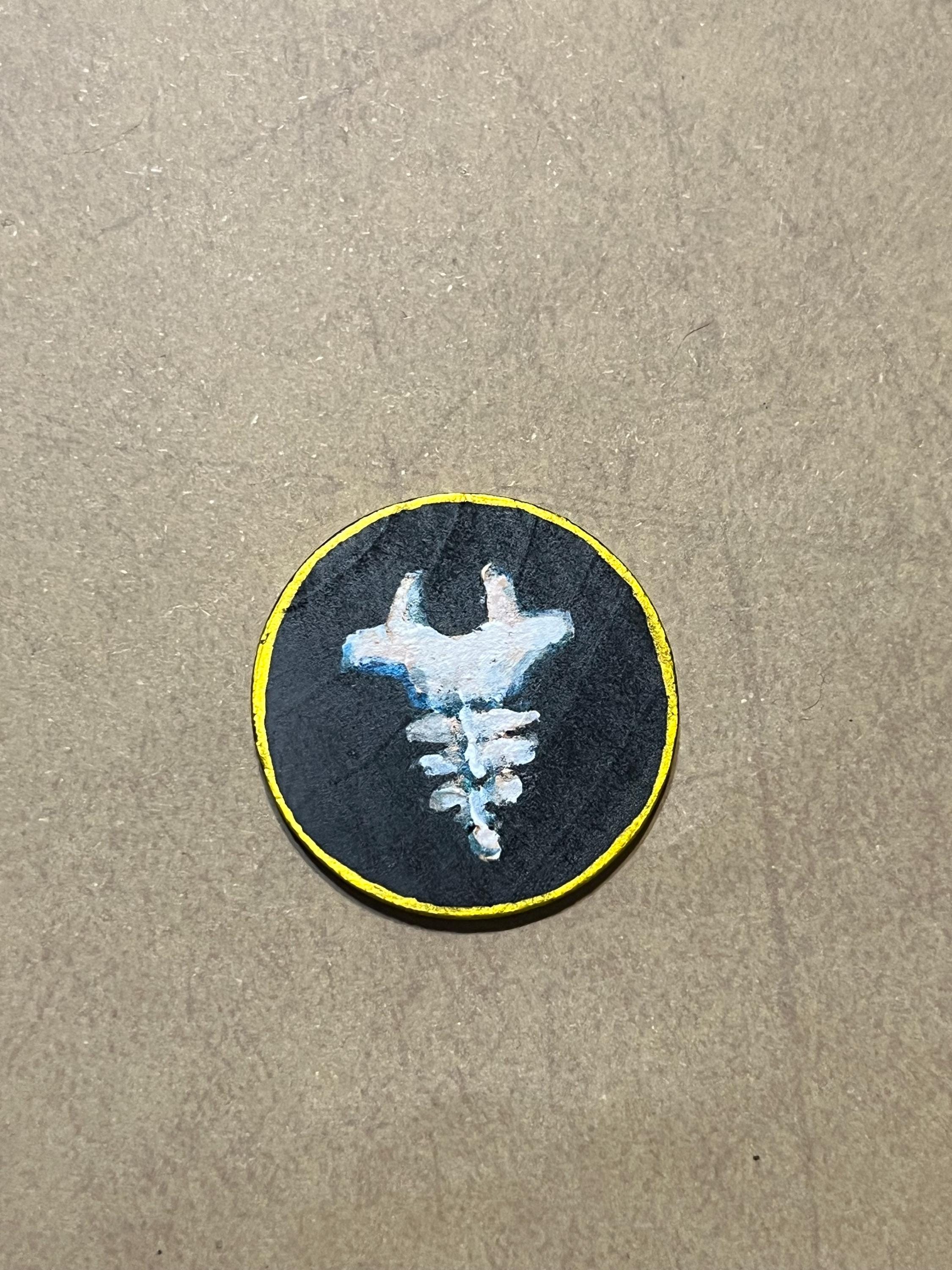 A round wooden token featuring a tailbone design with a gold border.