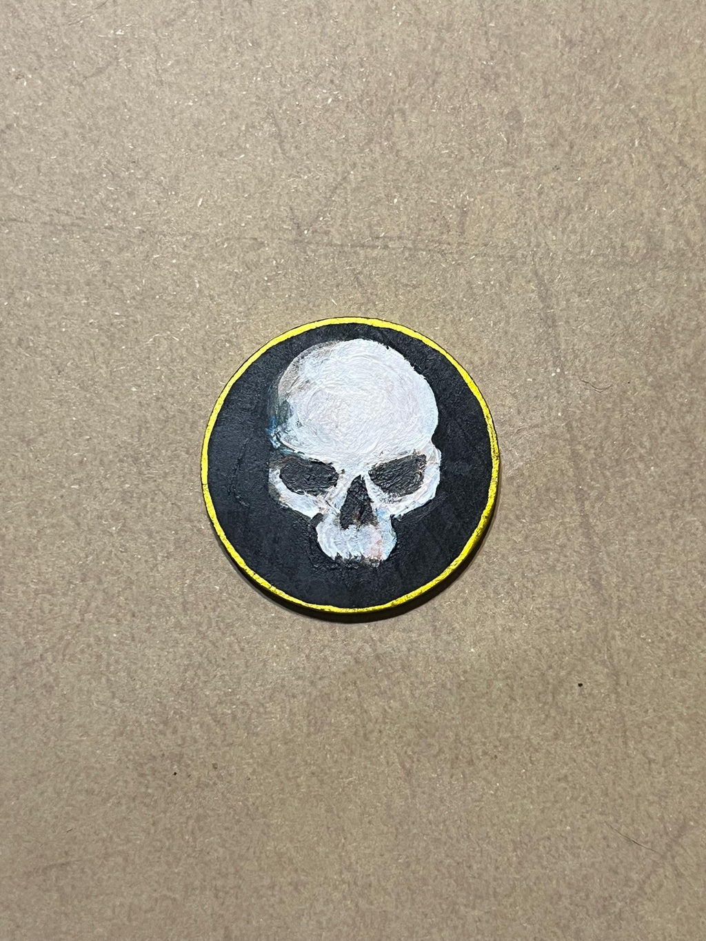 A round wooden token featuring a white skull design with a gold border.